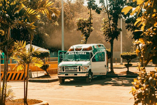 A parked ambulance in a sunny outdoor space, surrounded by trees and urban elements.